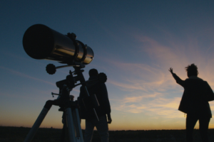 Télescope en premier plan avec deux personnes regardant le ciel